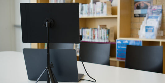 Flexsta portable monitor stand holding a portable monitor above a MacBook on a library desk